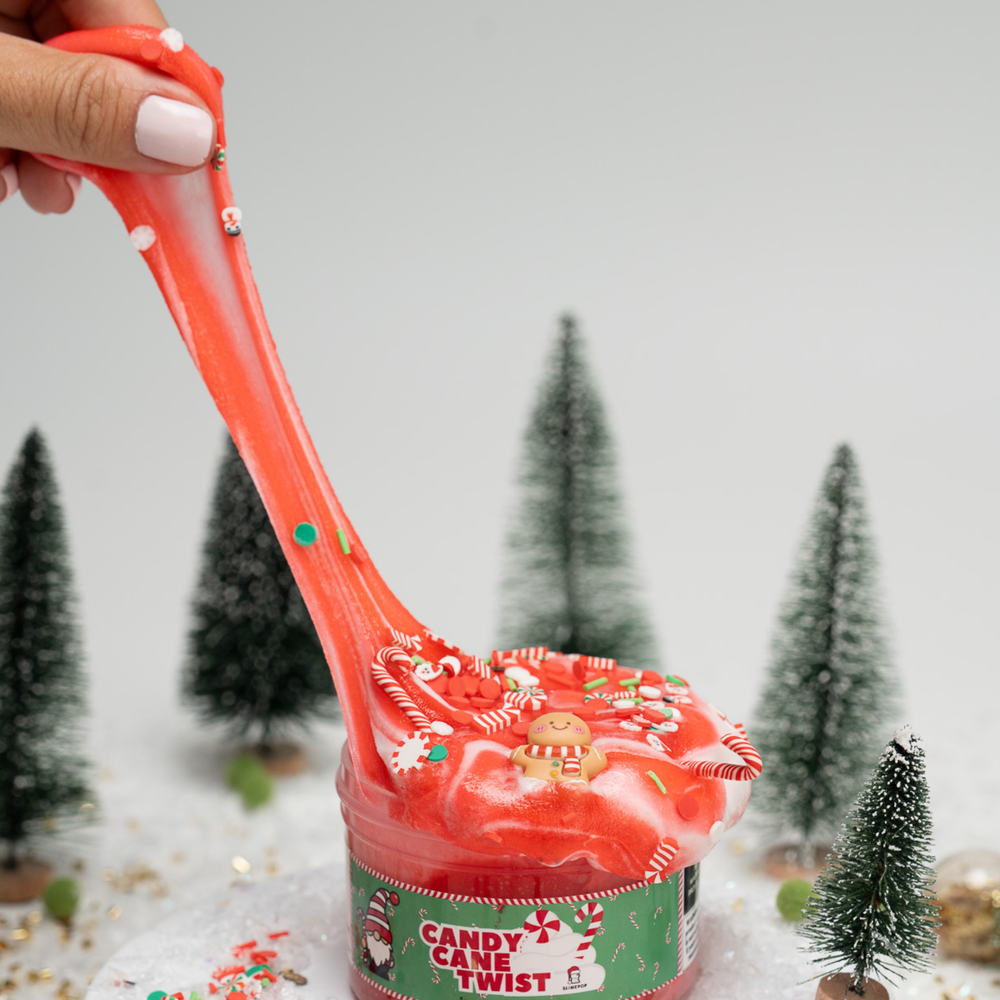 Candy cane twist slimepop  slime jar with a festive design, held by a hand against a snowy background with miniature trees.