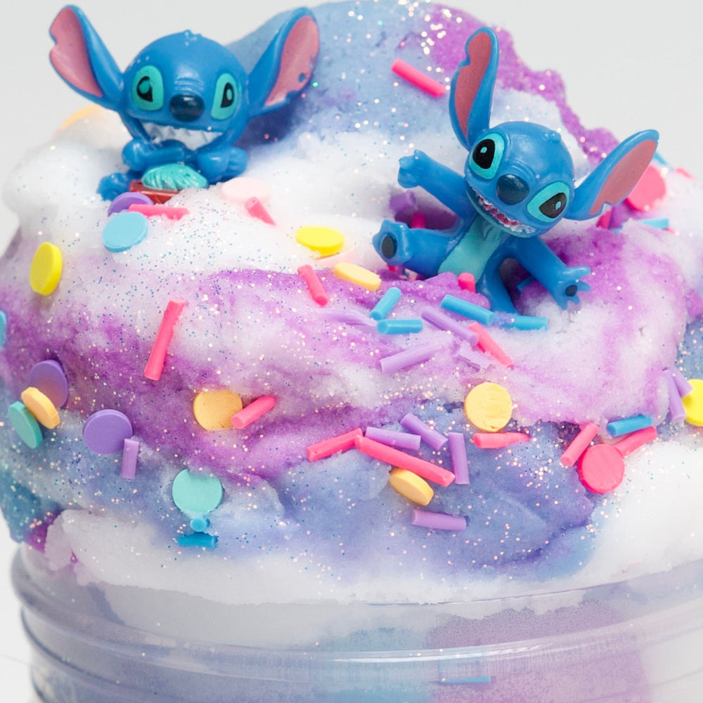 Two blue Stitch cartoon characters on a colorful, fluffy cloud slime with sprinkles.
Stitch in a Tub DIY slime kit featuring violet, blue, and white swirled cloud slime with two Stitch character charms and star sprinkles.