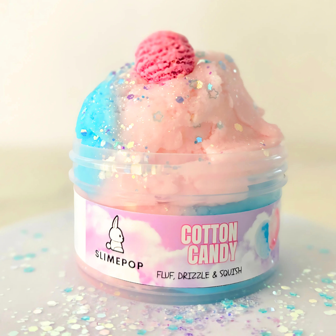 A container of Cotton Candy Slime with a pink and blue hue, decorated with a sprinkle mix and a charm resembling an ice cream scoop. The container is labeled with the brand SLIMEPOP