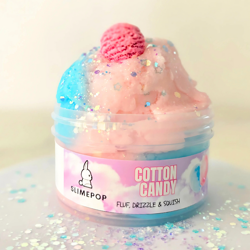 A container of Cotton Candy Slime with a pink and blue hue, decorated with a sprinkle mix and a charm resembling an ice cream scoop. The container is labeled with the brand SLIMEPOP