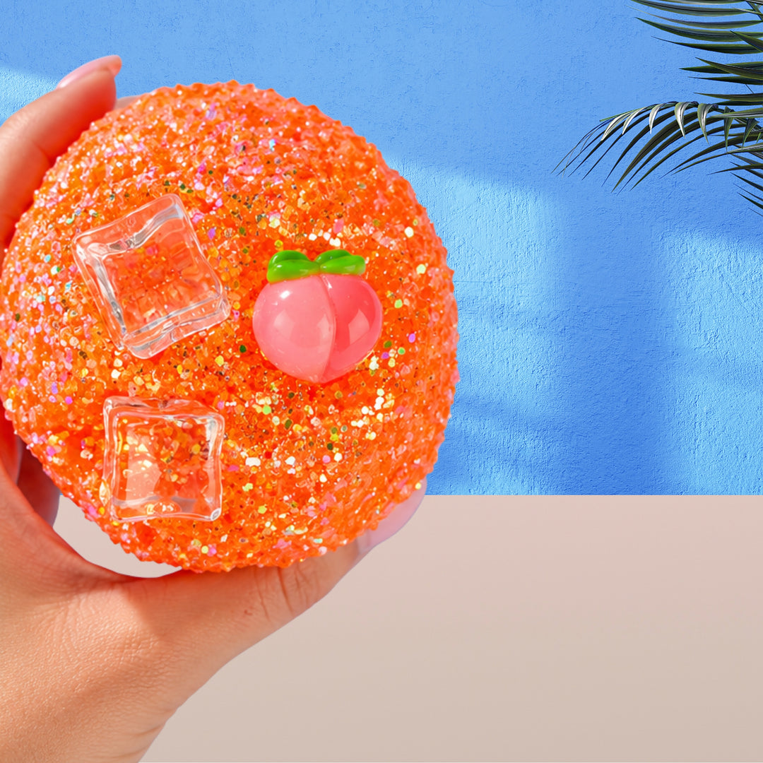 A hand holding Peach Slush Icee slime by Slimepop featuring a soft, frosty peach-colored texture inspired by a refreshing peach slushie. The slime has glitter, ice cube charms and a peach charm