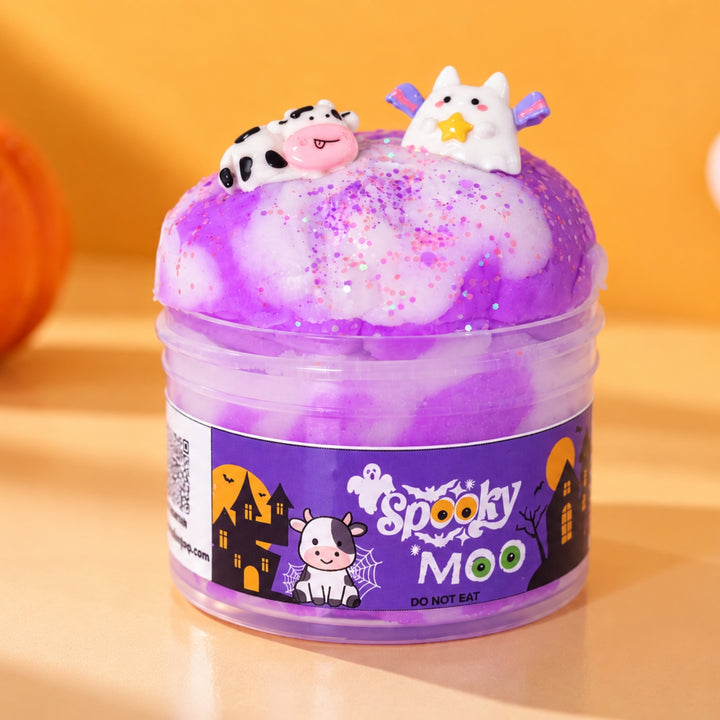 A clear plastic jar by Slimepop filled with purple and white cloud slime topped with a small cow and cat decoration, set against a warm orange background with a pumpkin partially visible on the left.